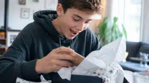jeune garçon adolescent ouvrant un cadeau d'anniversaire avec enthousiasme